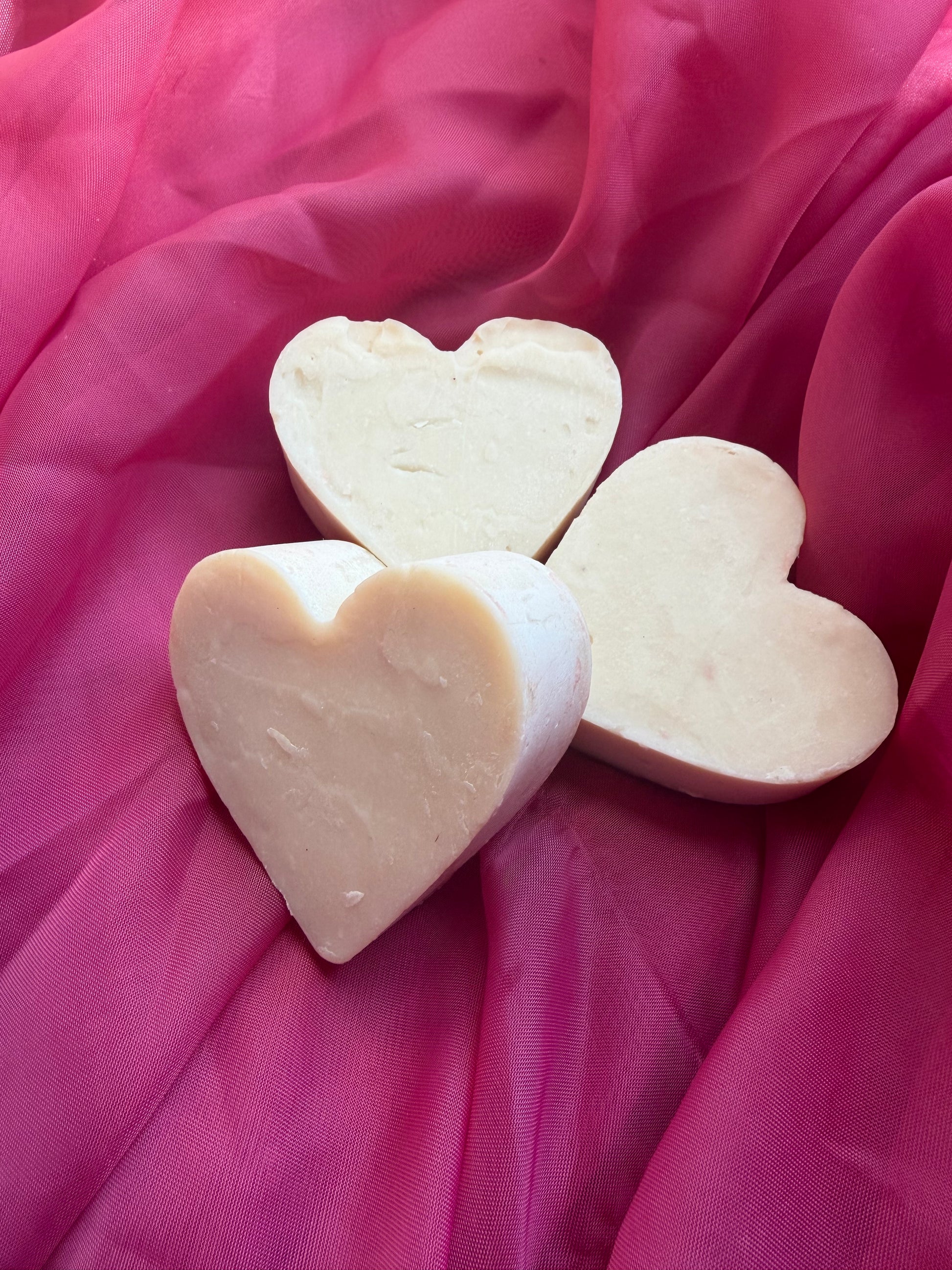 Three unfrosted heart-shaped soap bars on a pink fabric background