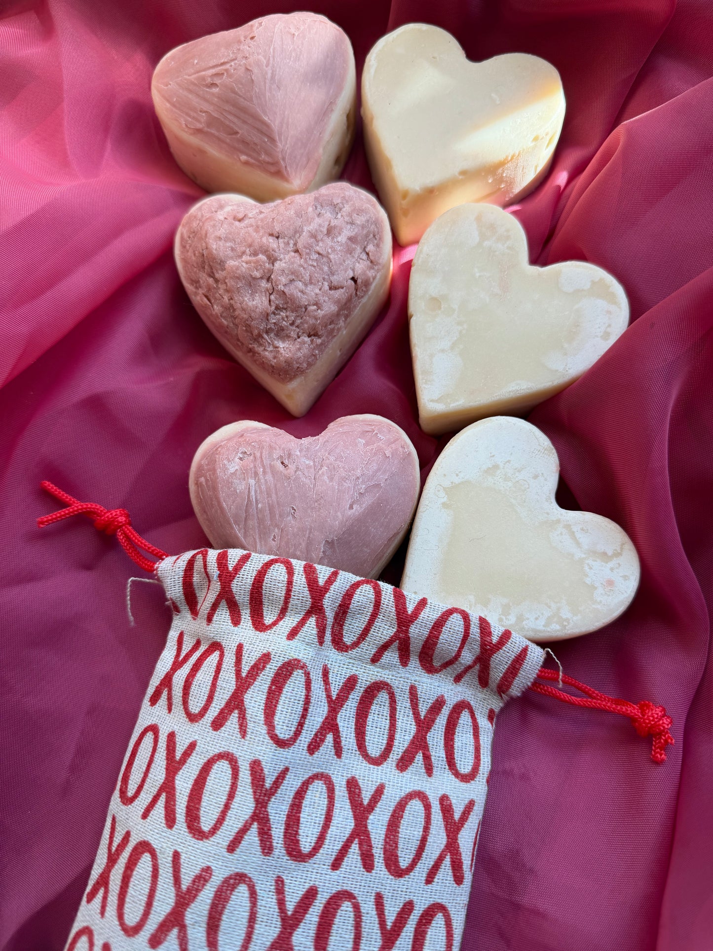 Heart-shaped soaps both frosted and unfrosted with a decorative bag on a pink fabric background